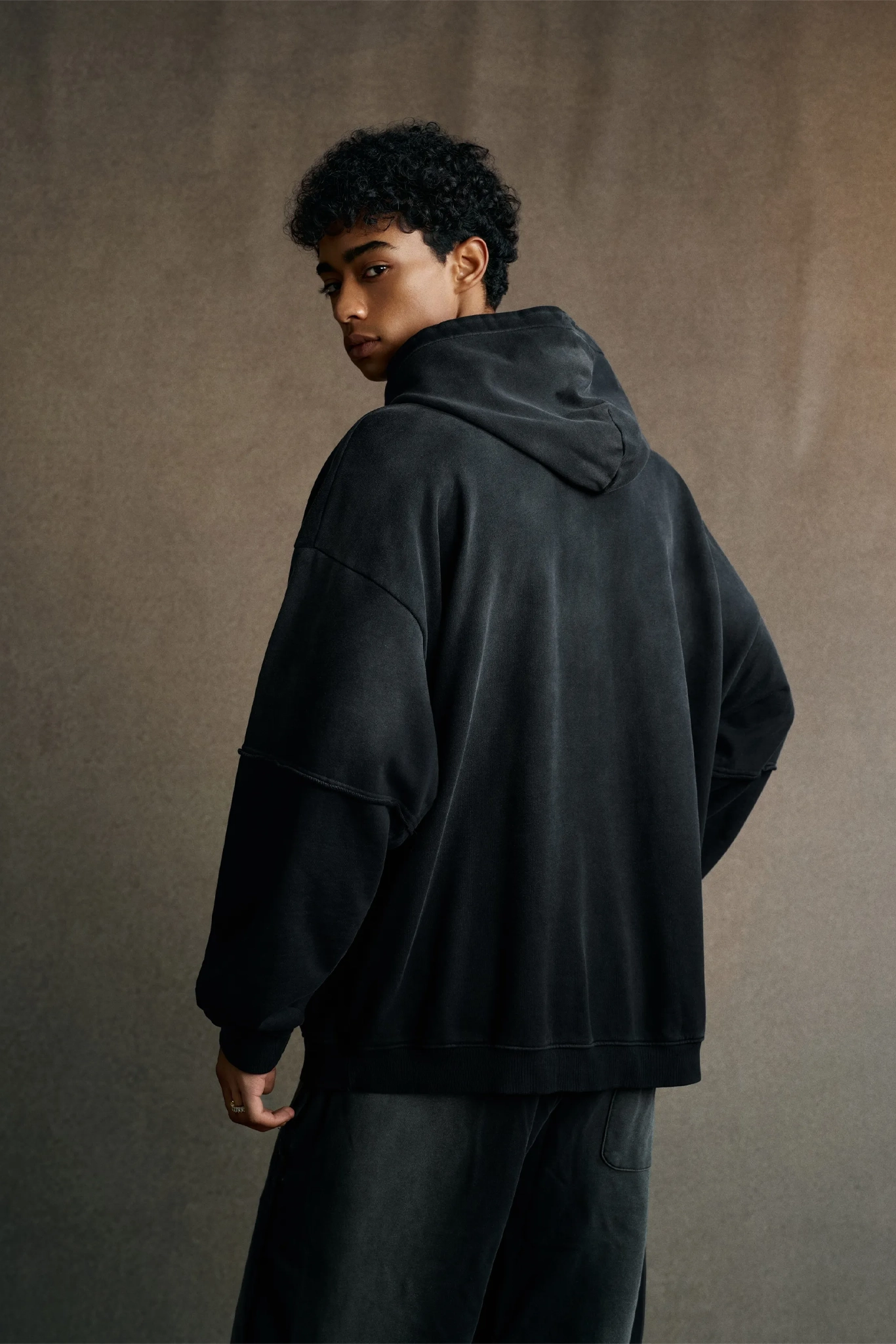 Person wearing a black hoodie and pants against a brown background