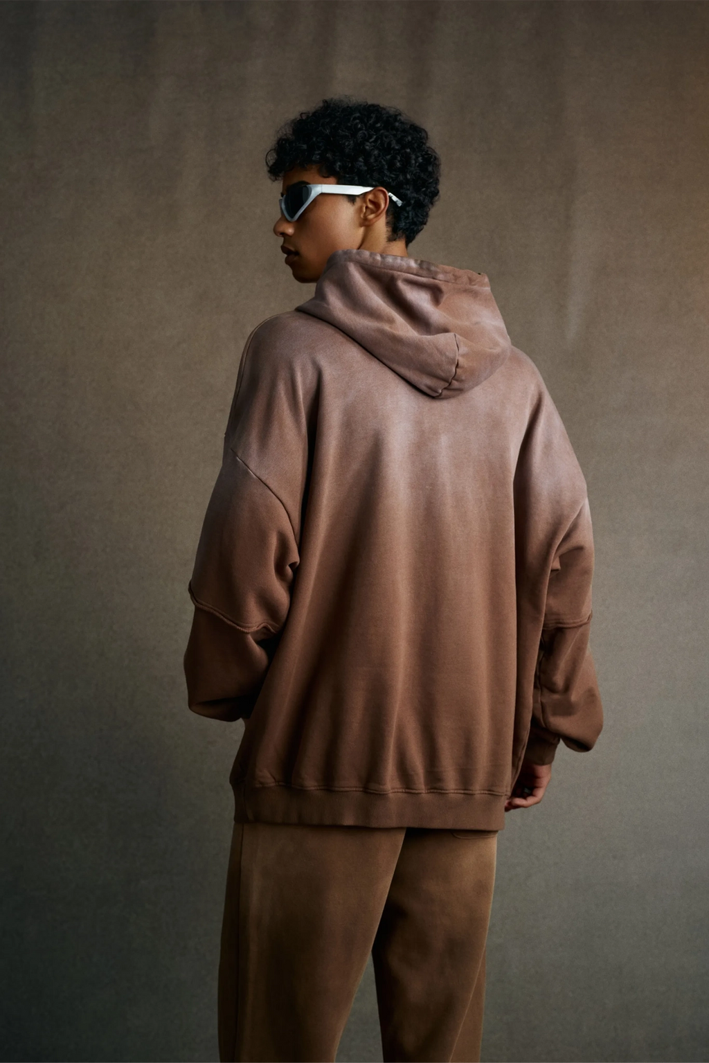 Person wearing a brown hoodie and pants against a plain background