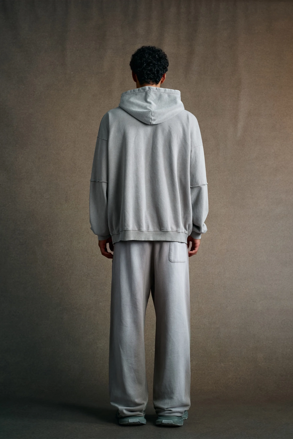 Person wearing a gray hoodie and pants against a plain background