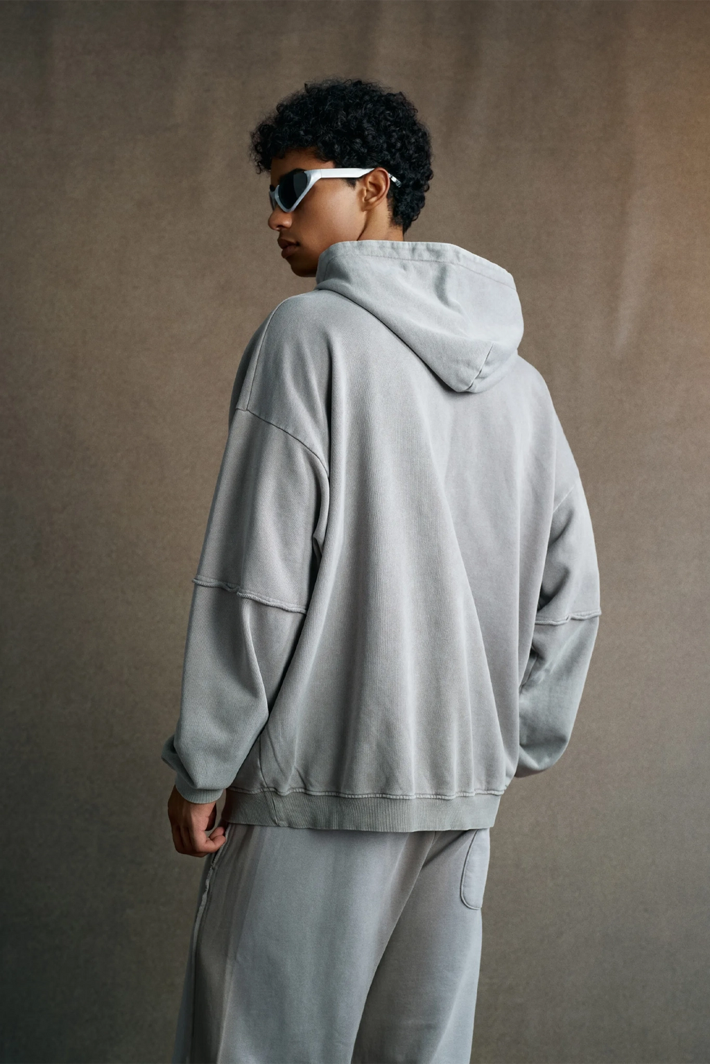 Person wearing a gray hoodie and pants against a brown background