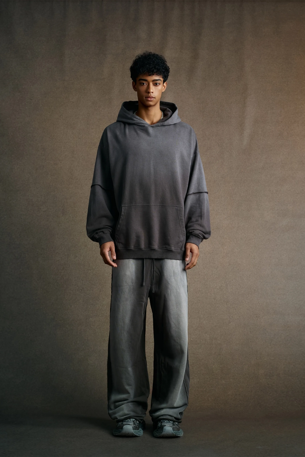 Person wearing a gray hoodie and pants against a brown background