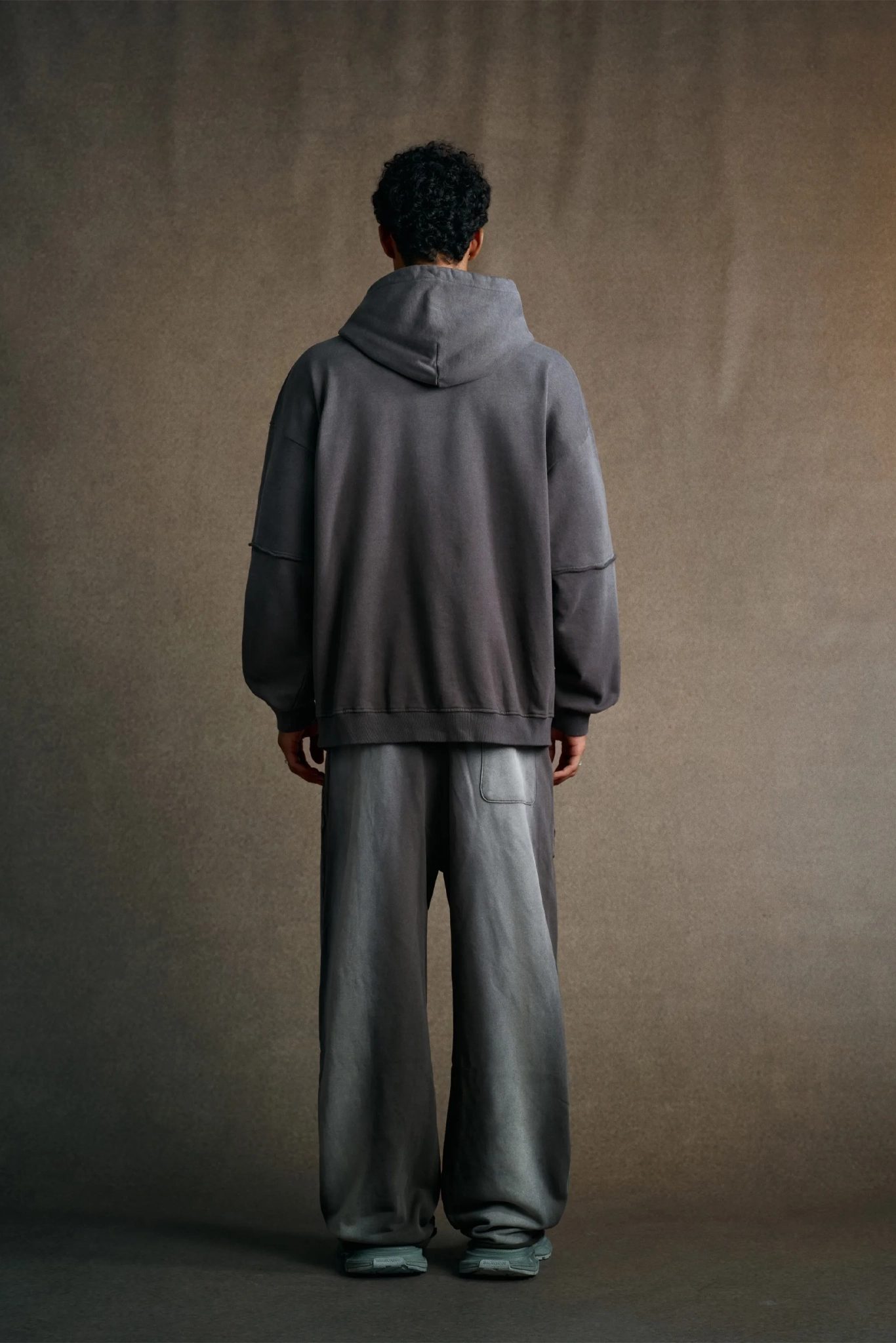 Person wearing a gray hoodie and pants against a brown background