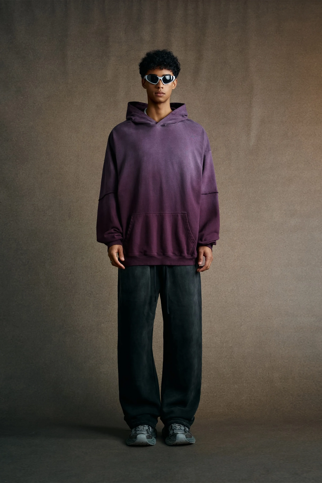 Person wearing a purple hoodie and dark pants against a brown background