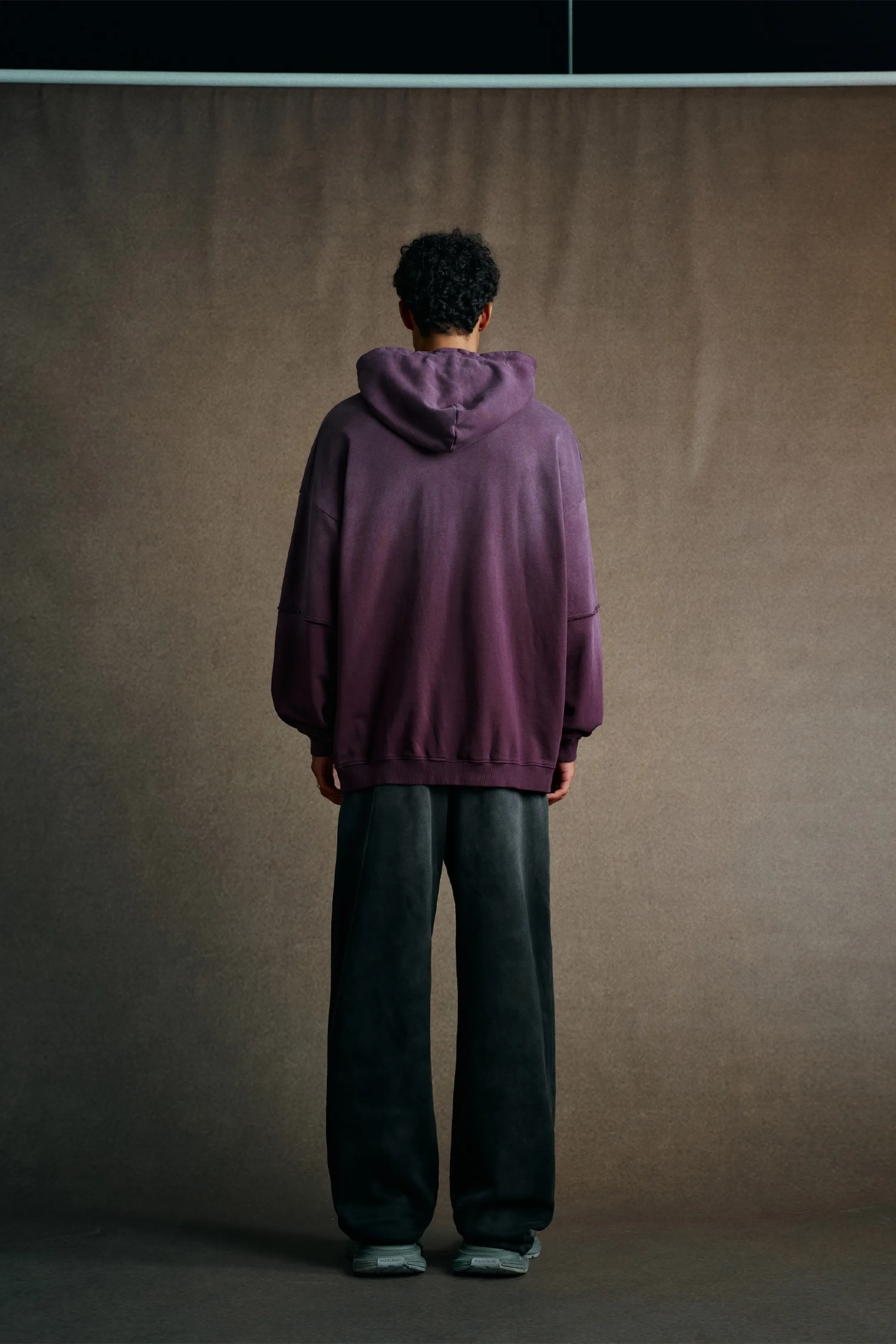 Person wearing a purple hoodie and dark pants standing against a plain background