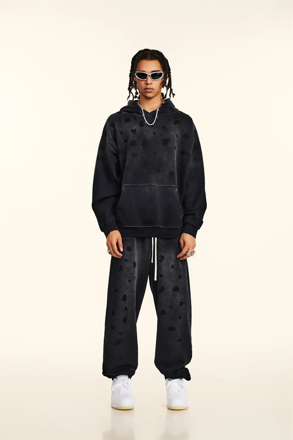 Person wearing a black hoodie and pants with heart patterns on a beige background