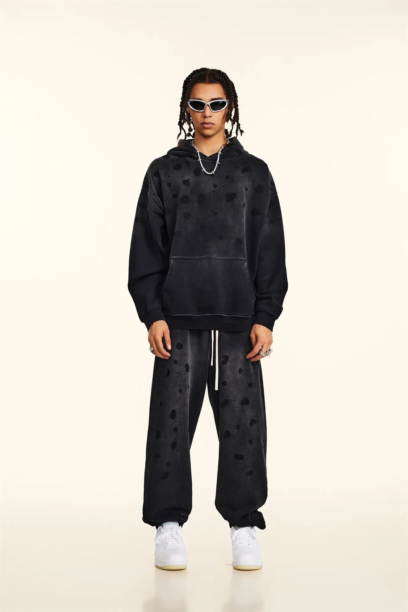 Person wearing a black hoodie and pants with heart patterns on a beige background