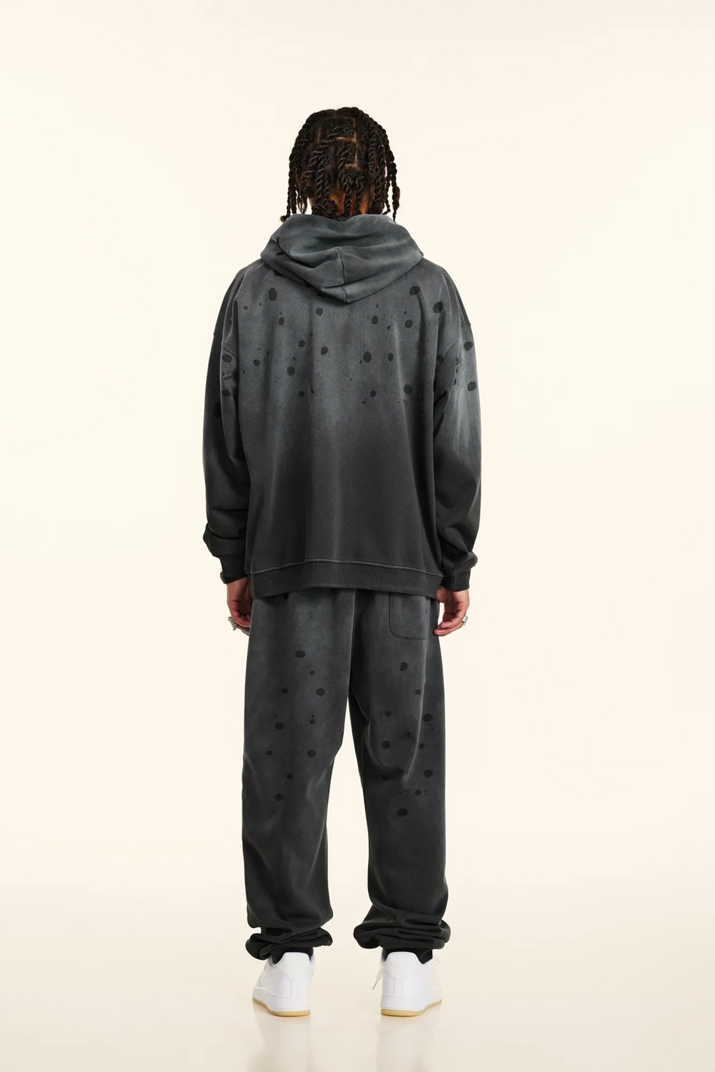 Person wearing a dark gray hoodie and pants set on a white background