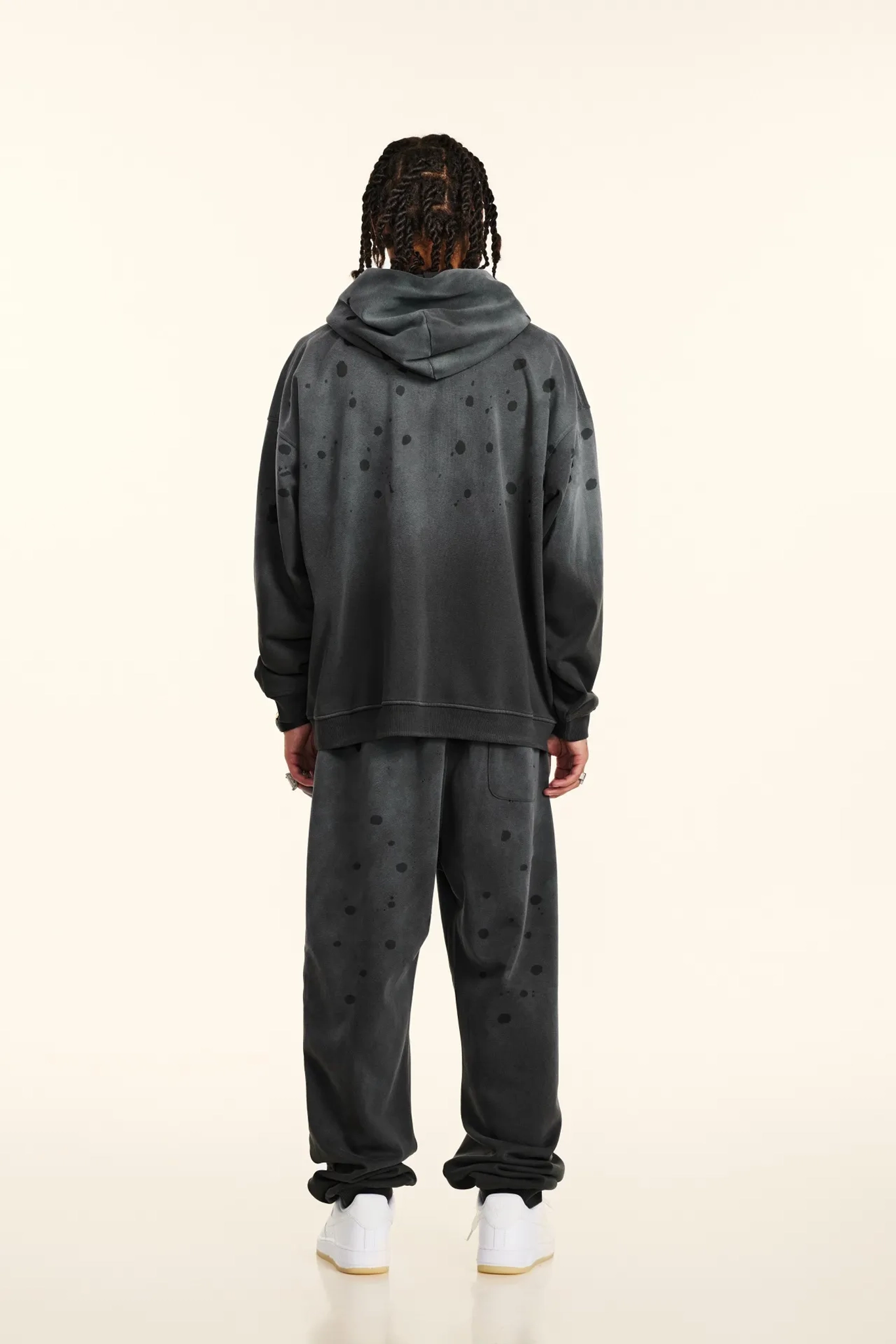 Person wearing a dark gray hoodie and pants set on a white background