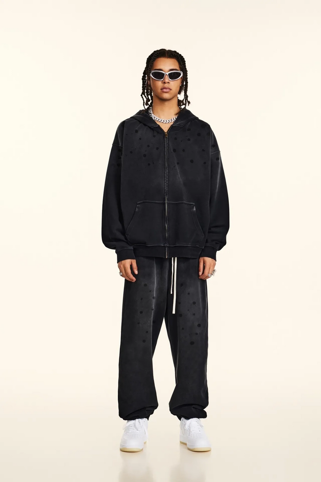 Person wearing a black hoodie and pants with white sneakers on a beige background