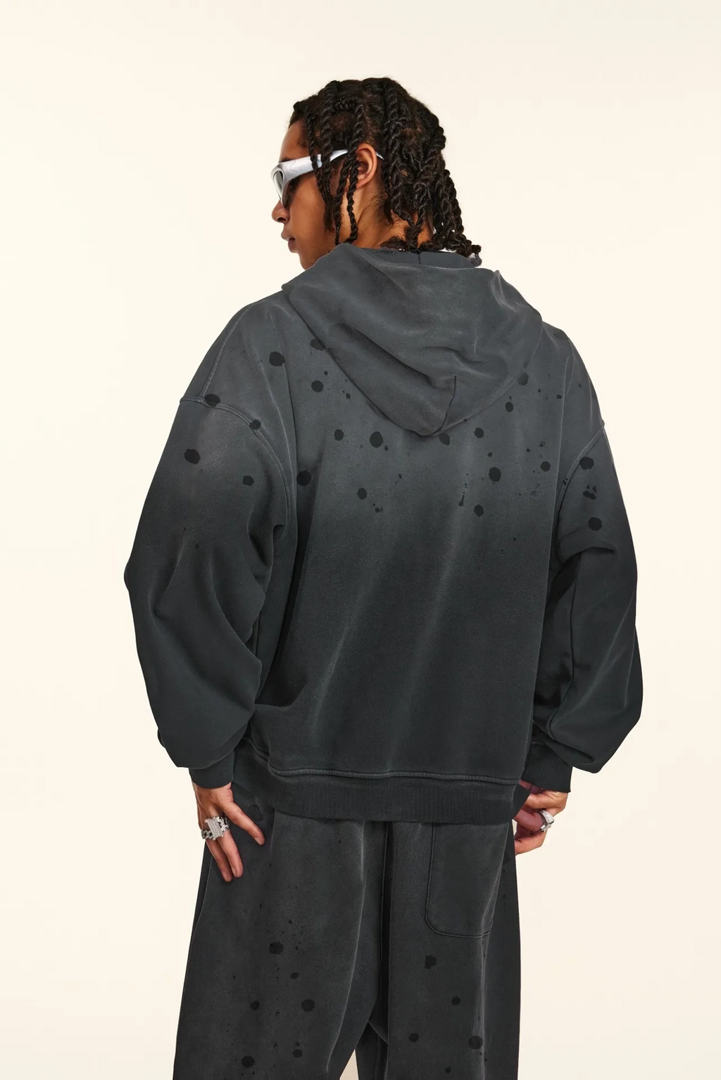 Person wearing a dark gray hoodie and pants with star patterns on a beige background