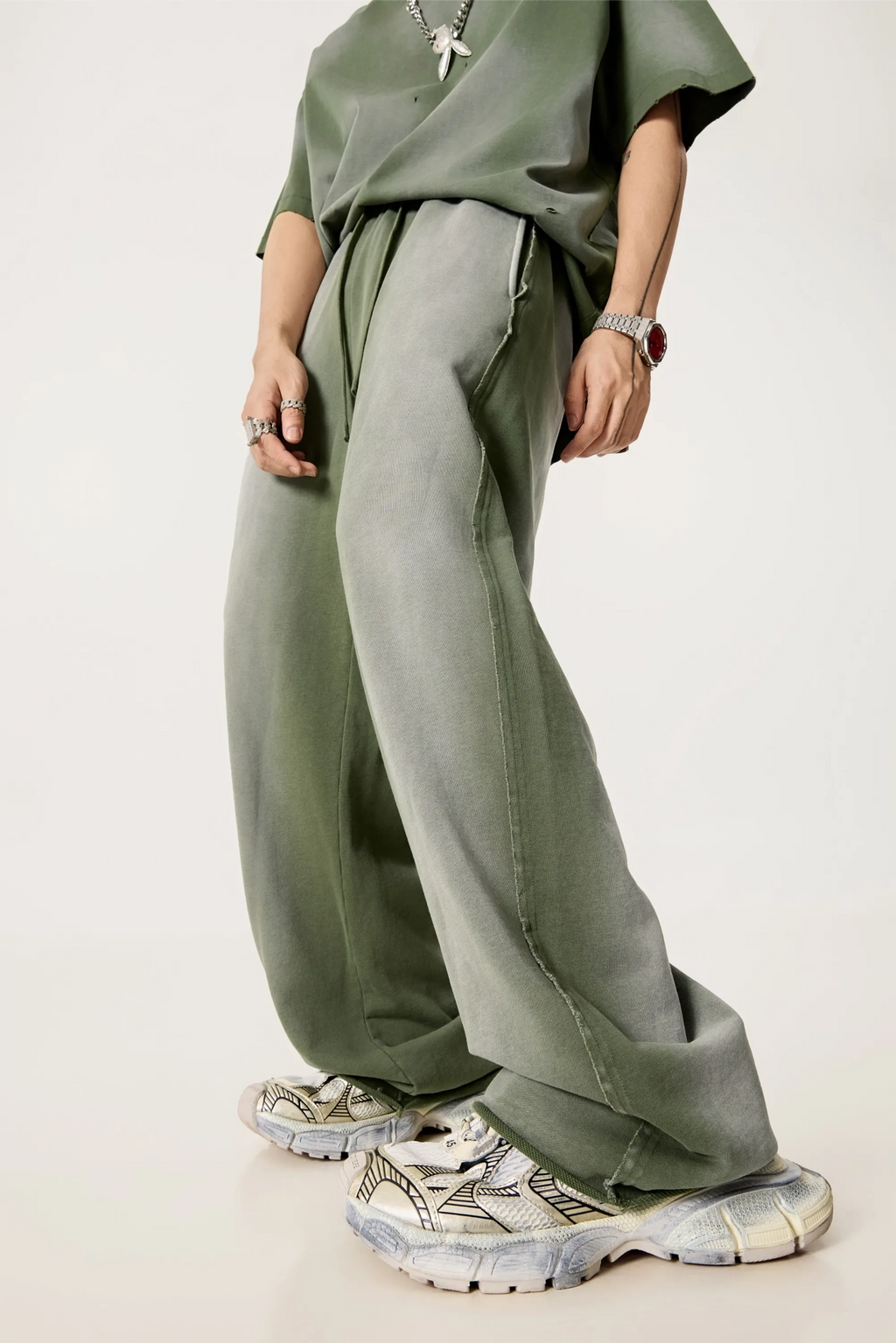 Person wearing a loose-fitting green outfit with wide-leg pants on a plain background