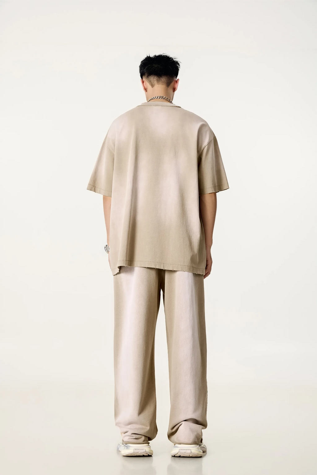 Person wearing a beige outfit standing against a white background