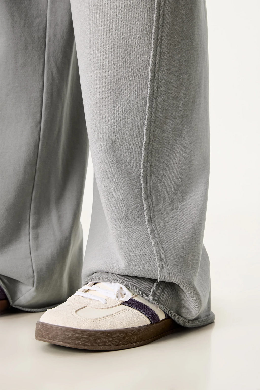 Person wearing light gray pants and a white sneaker with a brown sole on a light background