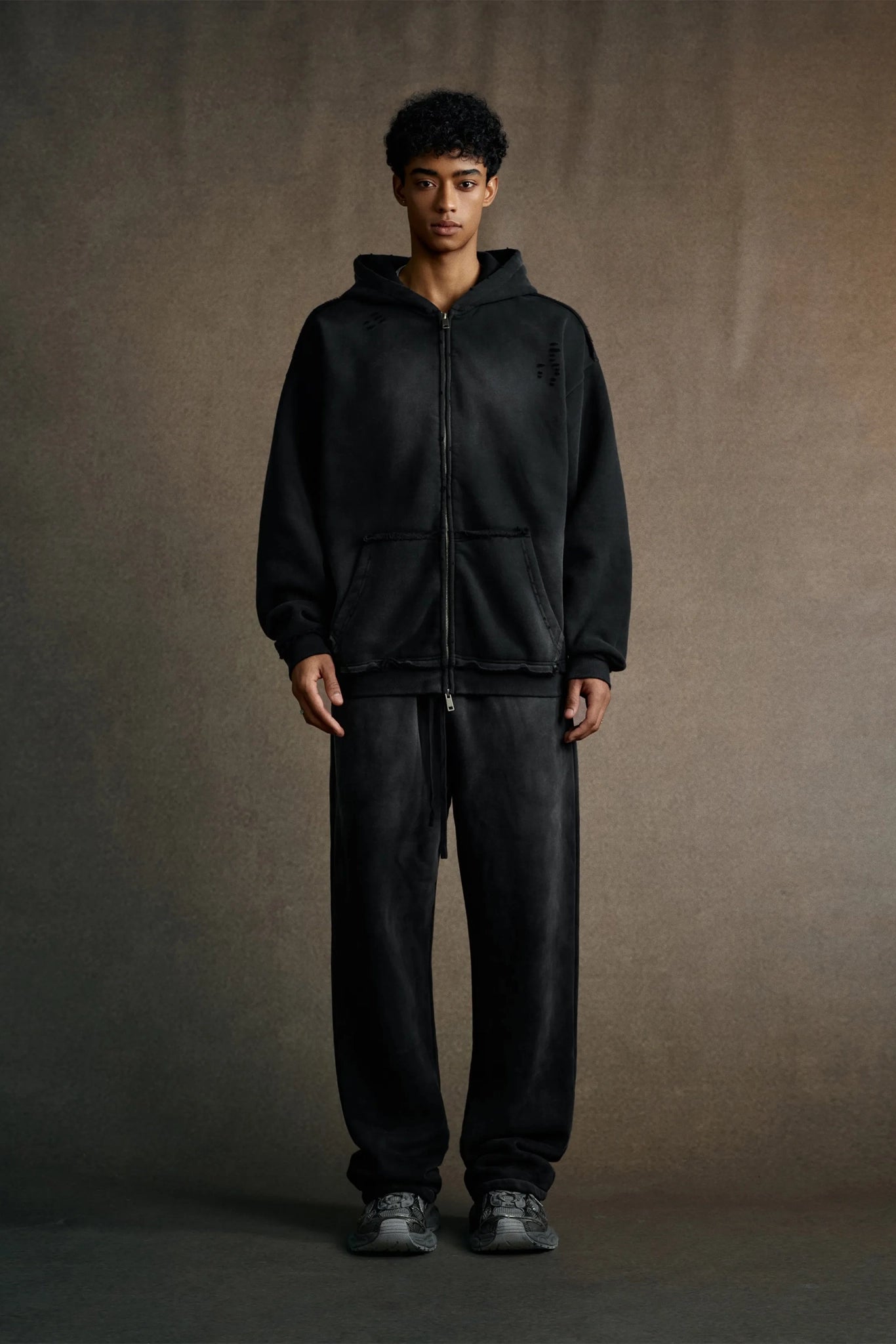 Person wearing a black hoodie and pants against a brown background