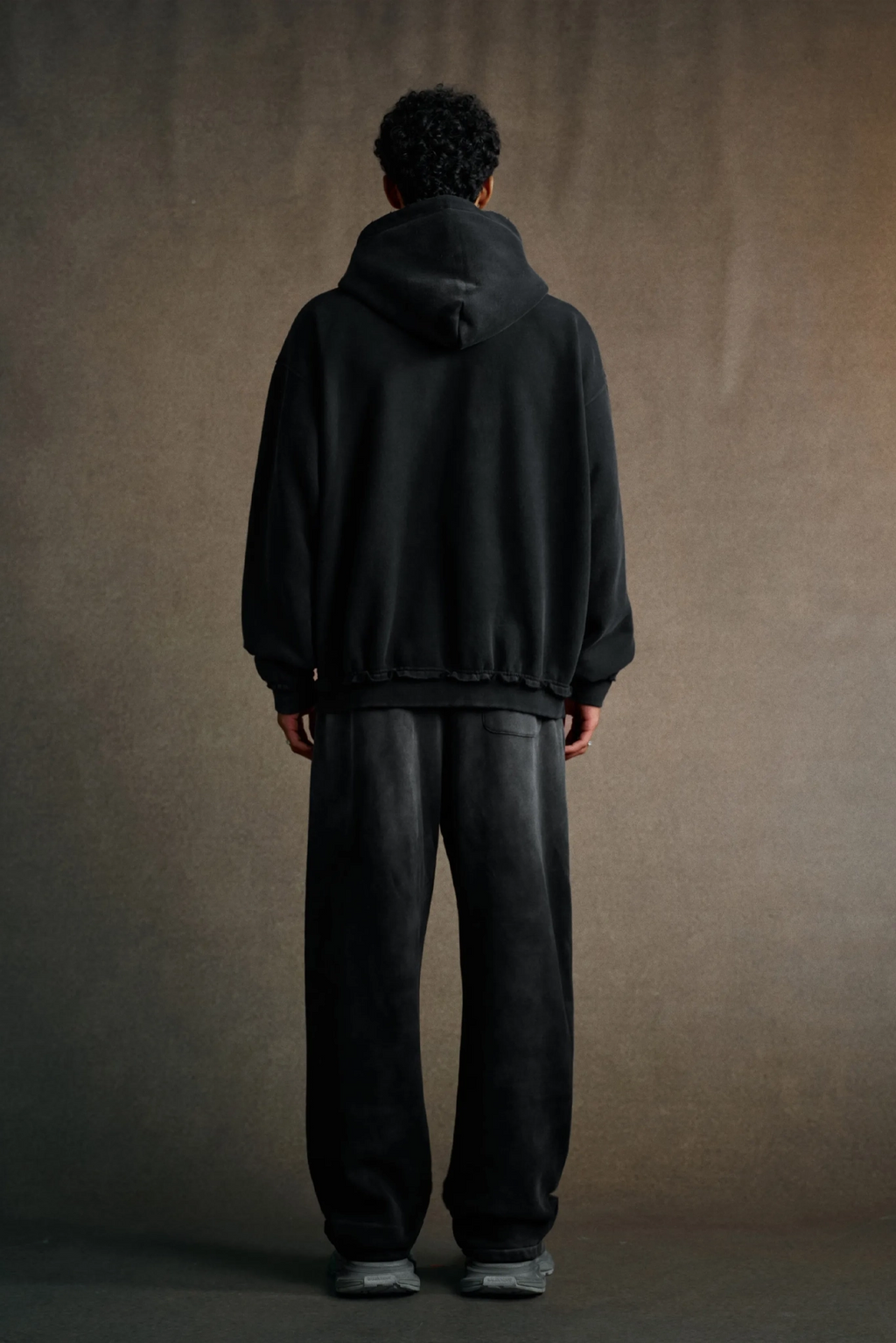 Person wearing a black hoodie and pants against a brown background