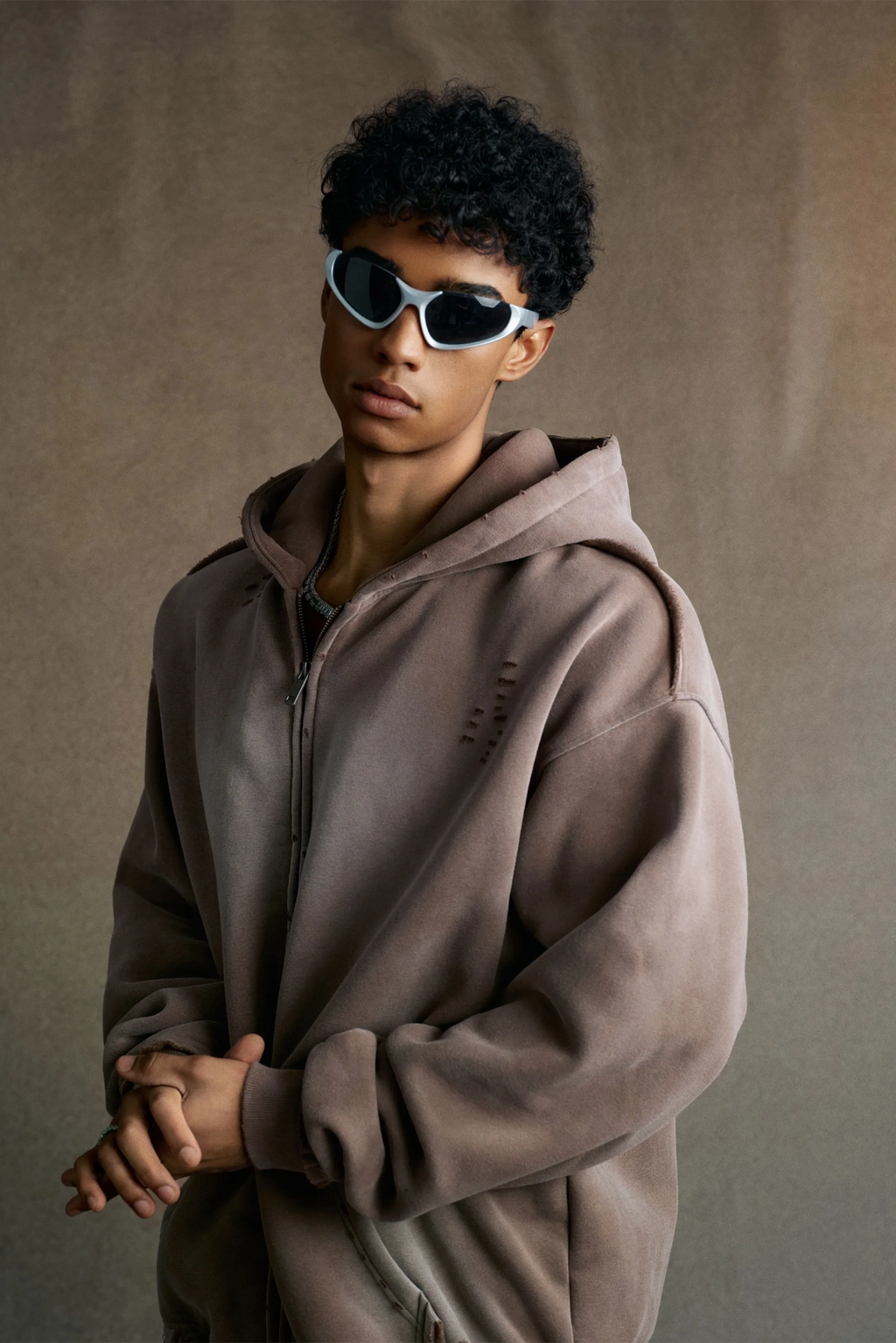 Person wearing a brown hoodie and sunglasses against a plain background