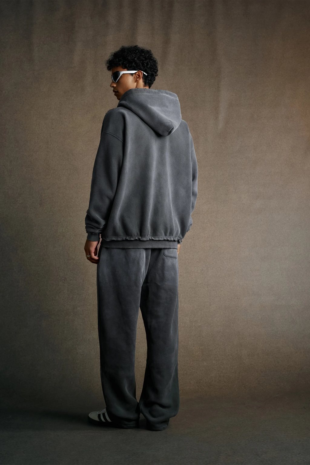 Person wearing a gray hoodie and pants against a brown background