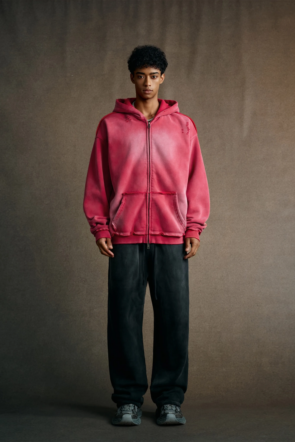 Person wearing a pink hoodie and dark pants against a plain background