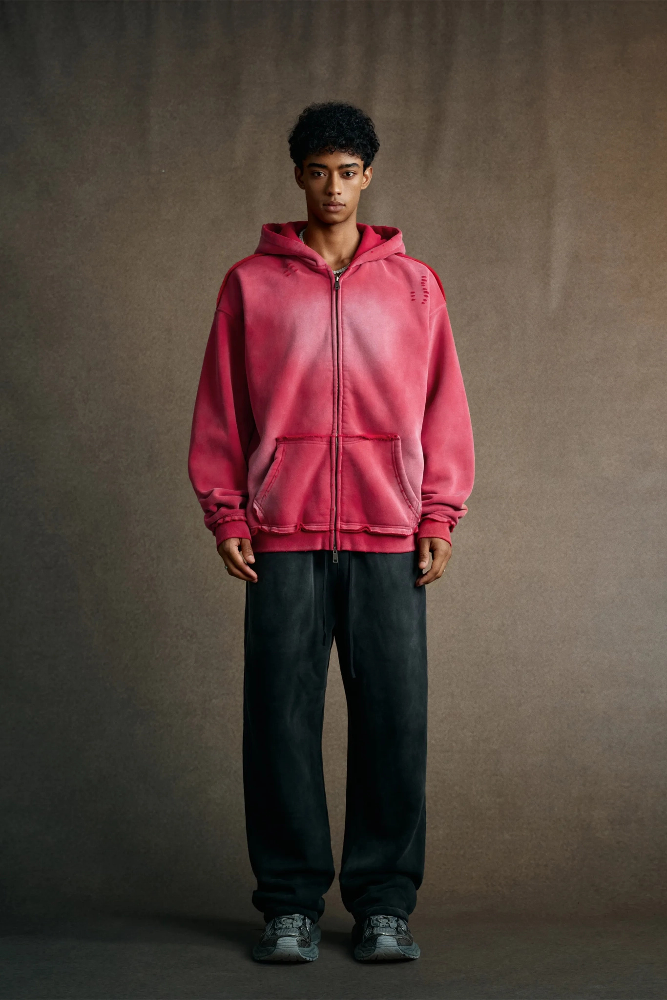 Person wearing a pink hoodie and dark pants against a plain background