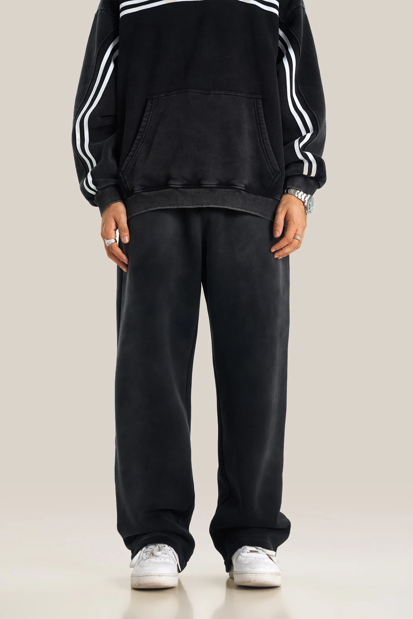 Person wearing a black tracksuit with white stripes on a beige background