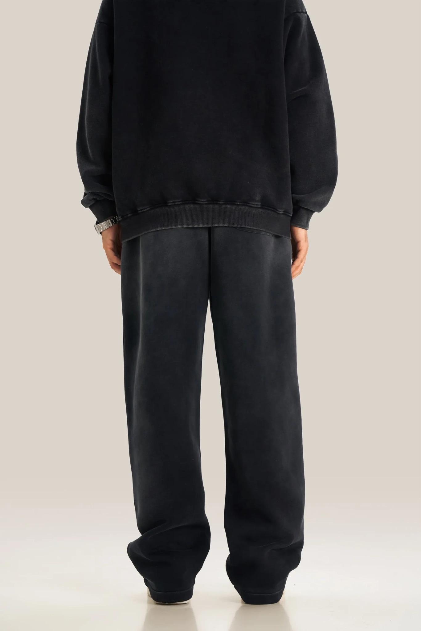 Person wearing a black sweatshirt and black pants on a plain background