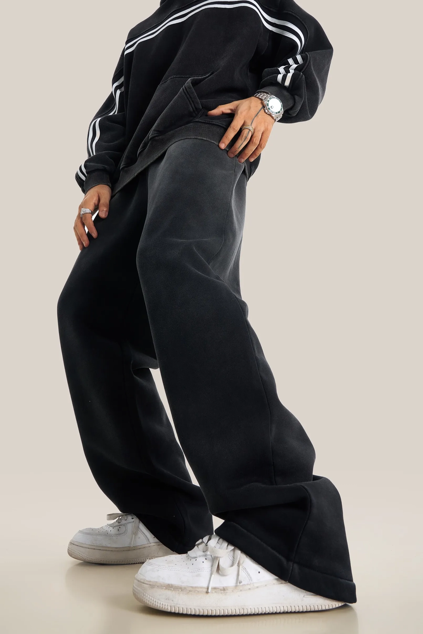 Person wearing a black tracksuit with white stripes and white sneakers on a beige background