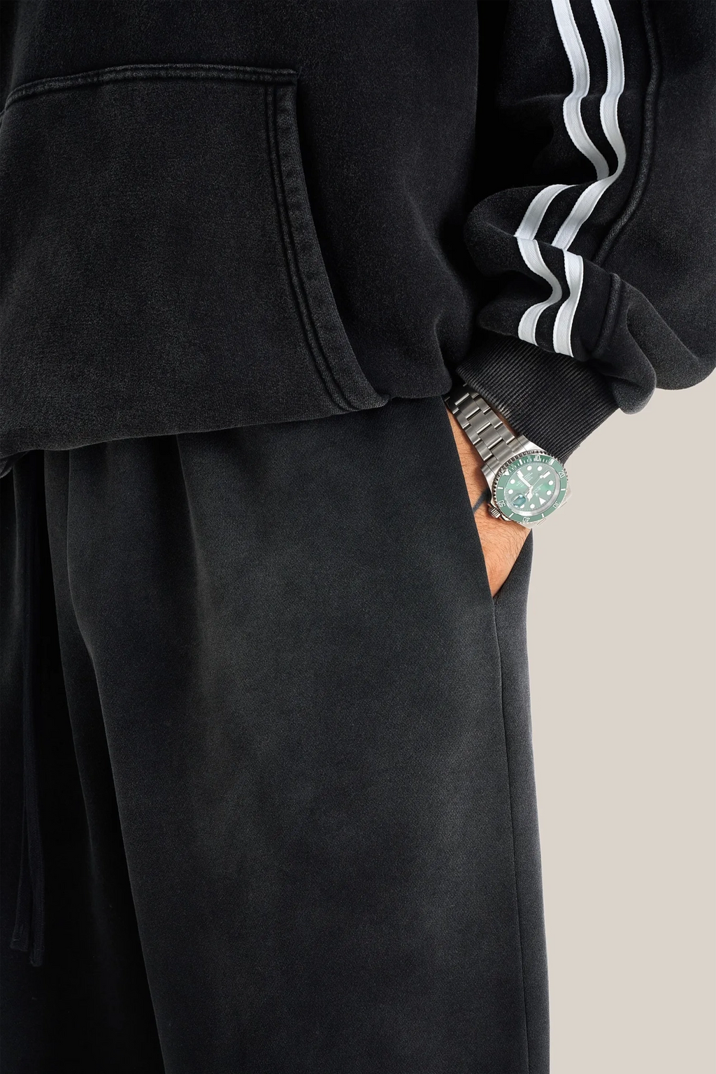 Person wearing a black outfit with white stripes on the sleeve, holding a phone in a pocket.