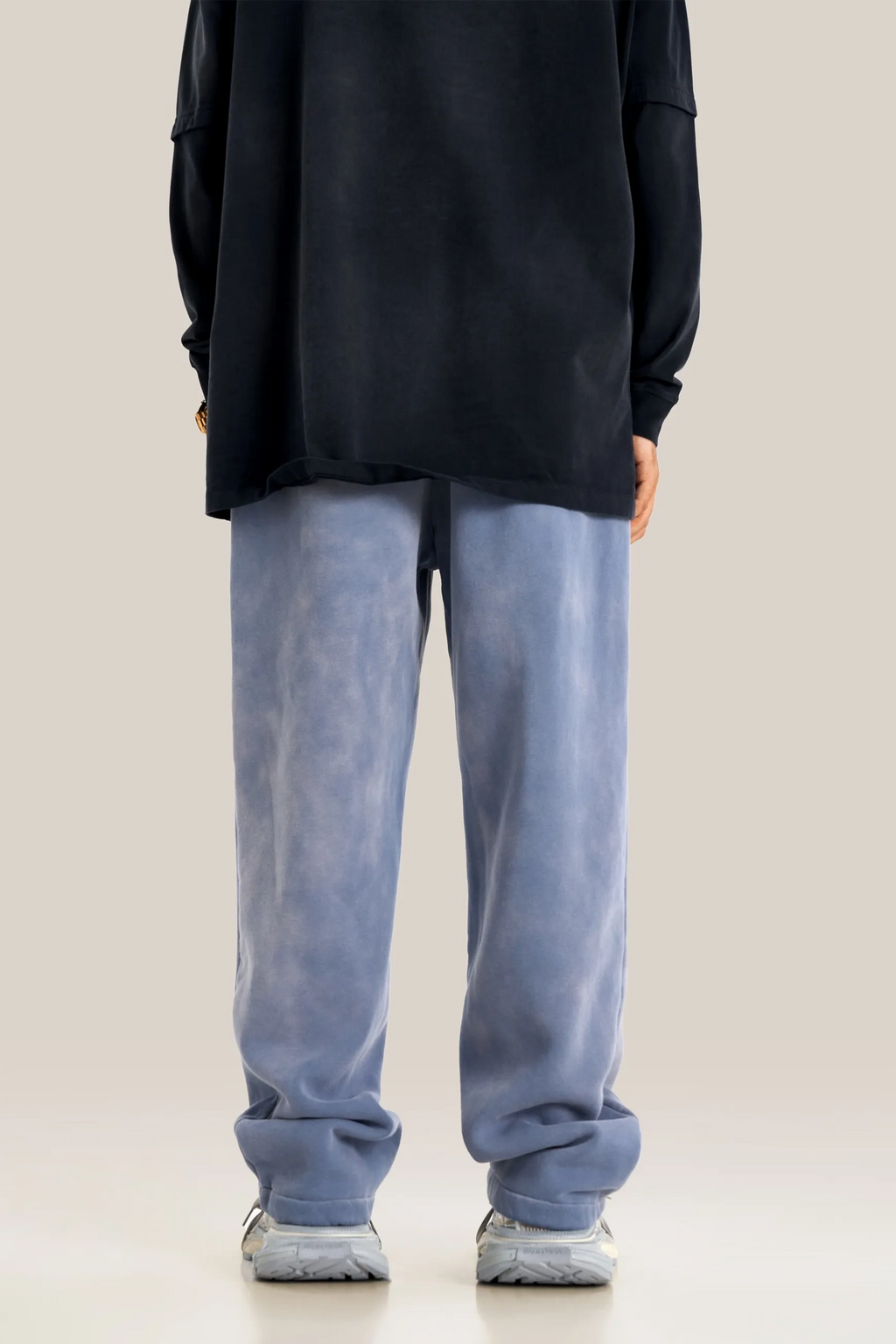 Person wearing a black oversized shirt and light blue jeans on a beige background