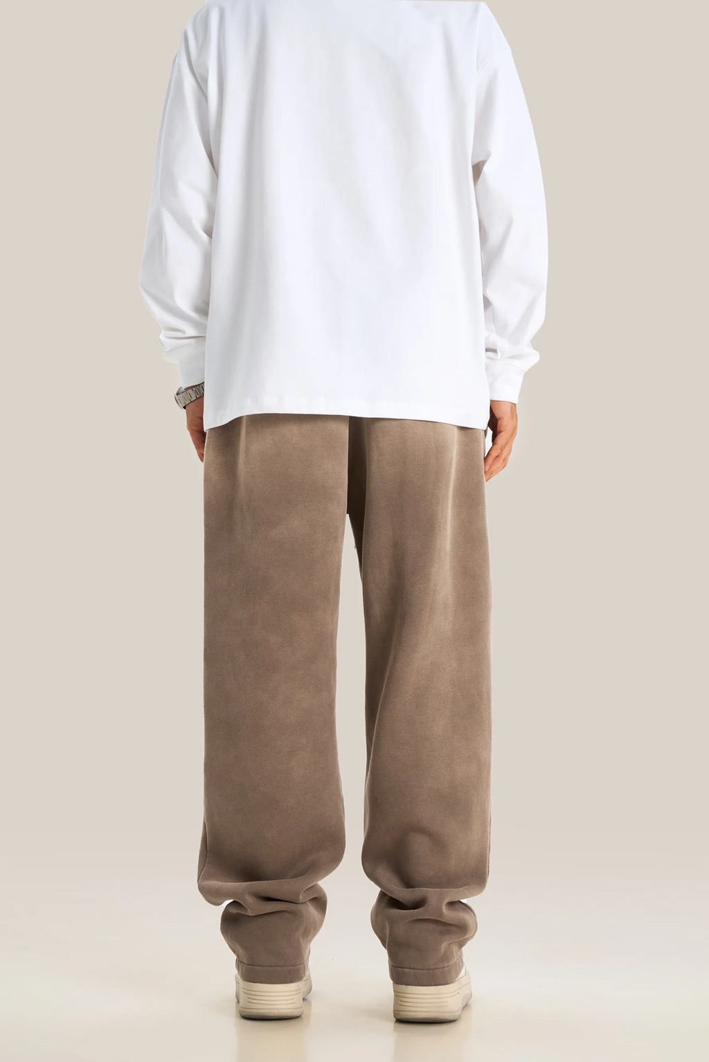 Person wearing a white sweatshirt and brown pants on a beige background