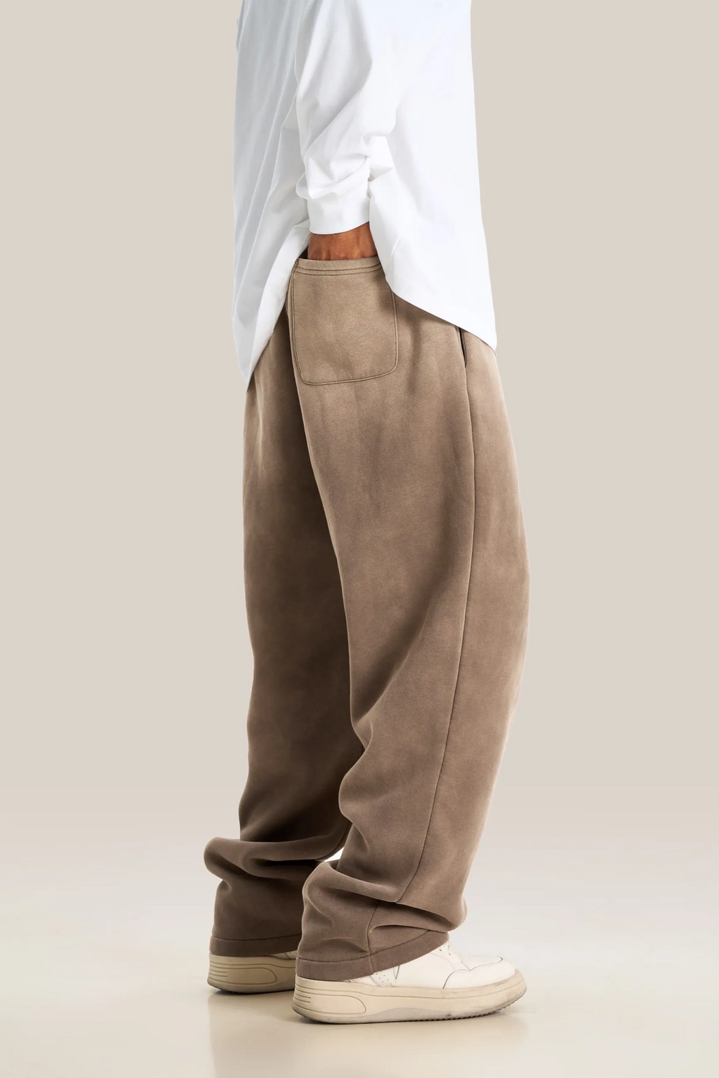 Person wearing brown pants and a white shirt on a plain background