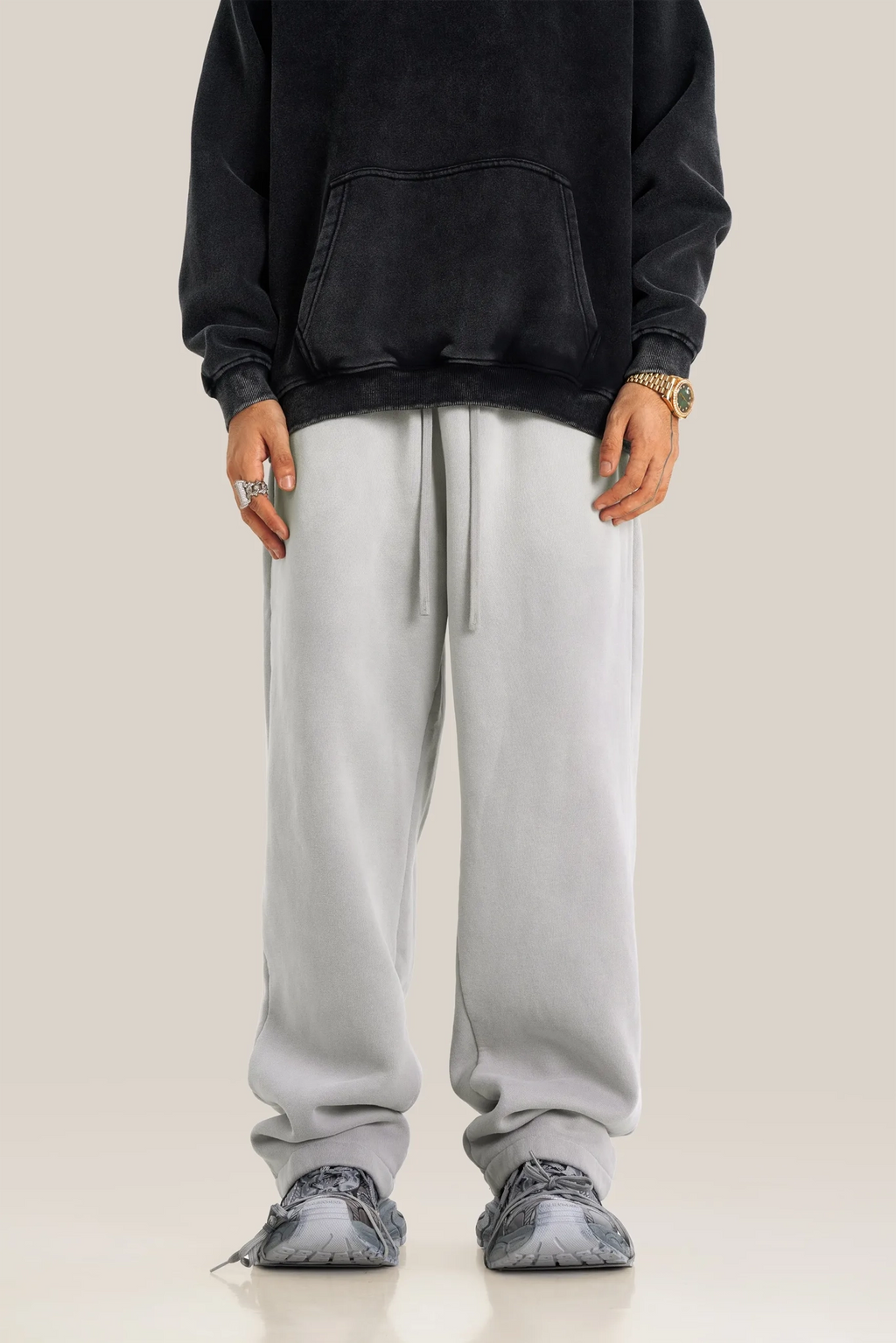 Person wearing a black hoodie and gray sweatpants on a plain background