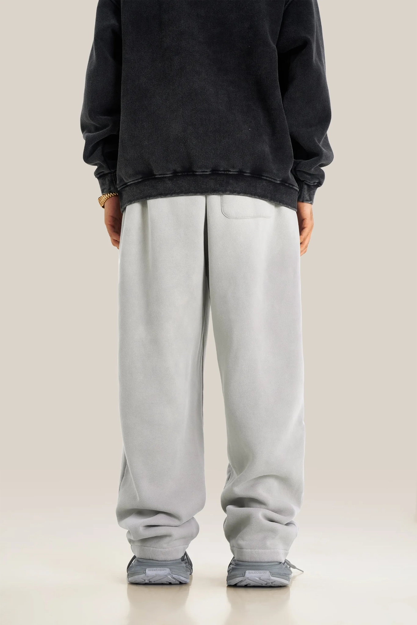 Person wearing a black sweatshirt and light gray pants on a beige background