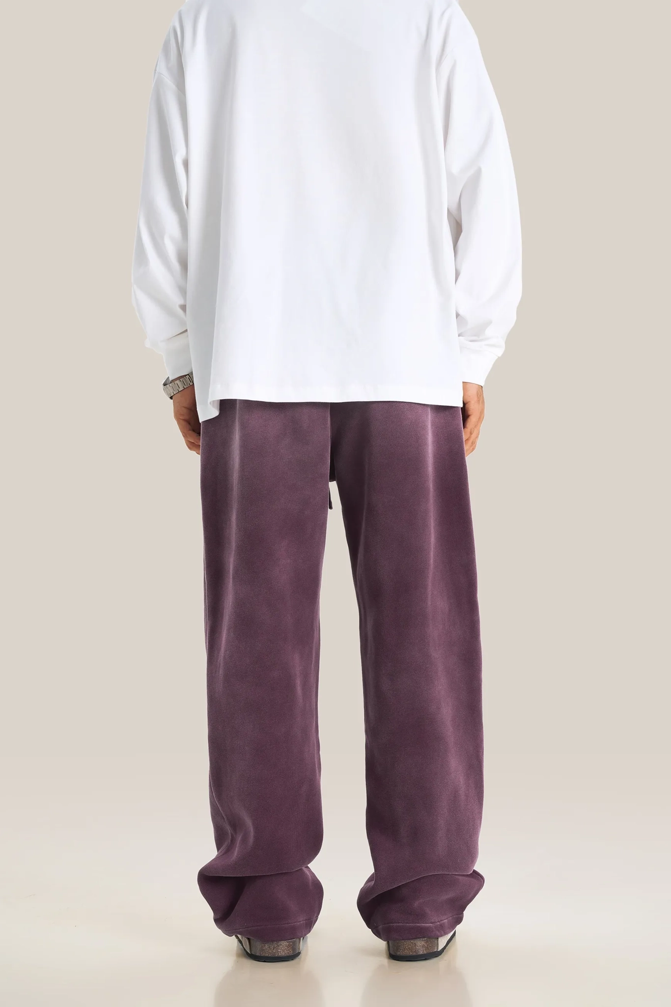 Person wearing a white shirt and purple pants on a beige background