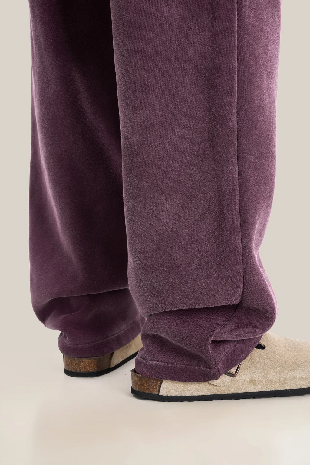 Purple velvet pants worn with beige shoes on a neutral background