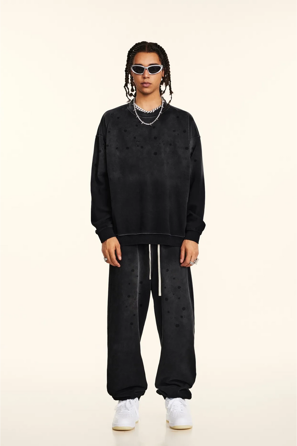 Person wearing a black oversized sweatshirt and pants with white sneakers on a beige background