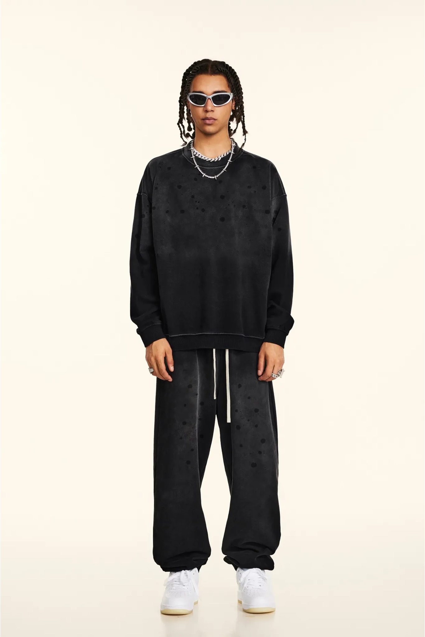 Person wearing a black oversized sweatshirt and pants with white sneakers on a beige background