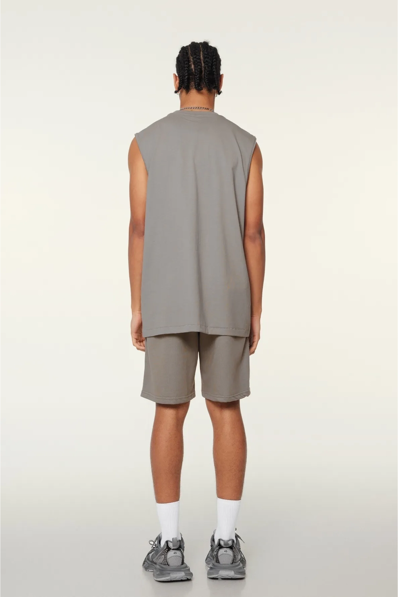 Person wearing a sleeveless gray top and shorts on a white background