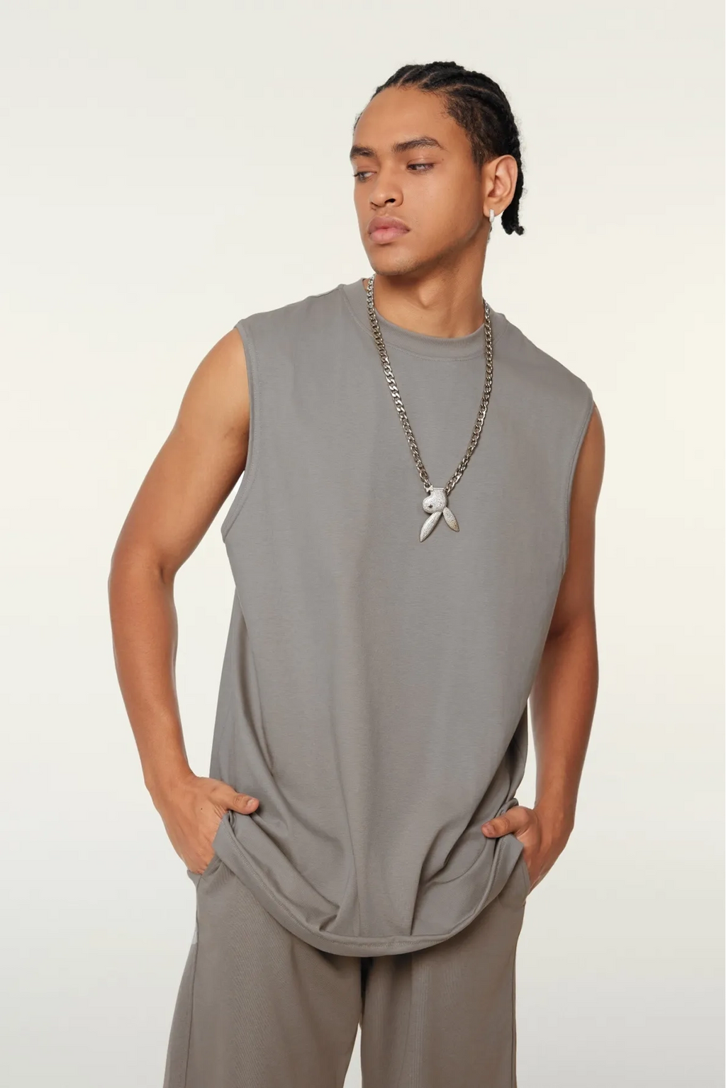 Man wearing a sleeveless gray top and beige pants against a white background