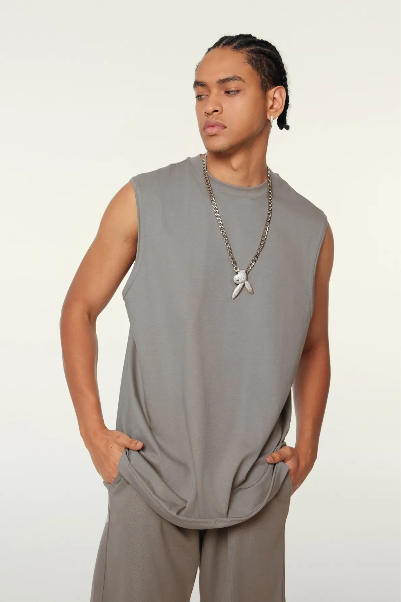 Man wearing a sleeveless gray top and beige pants against a white background