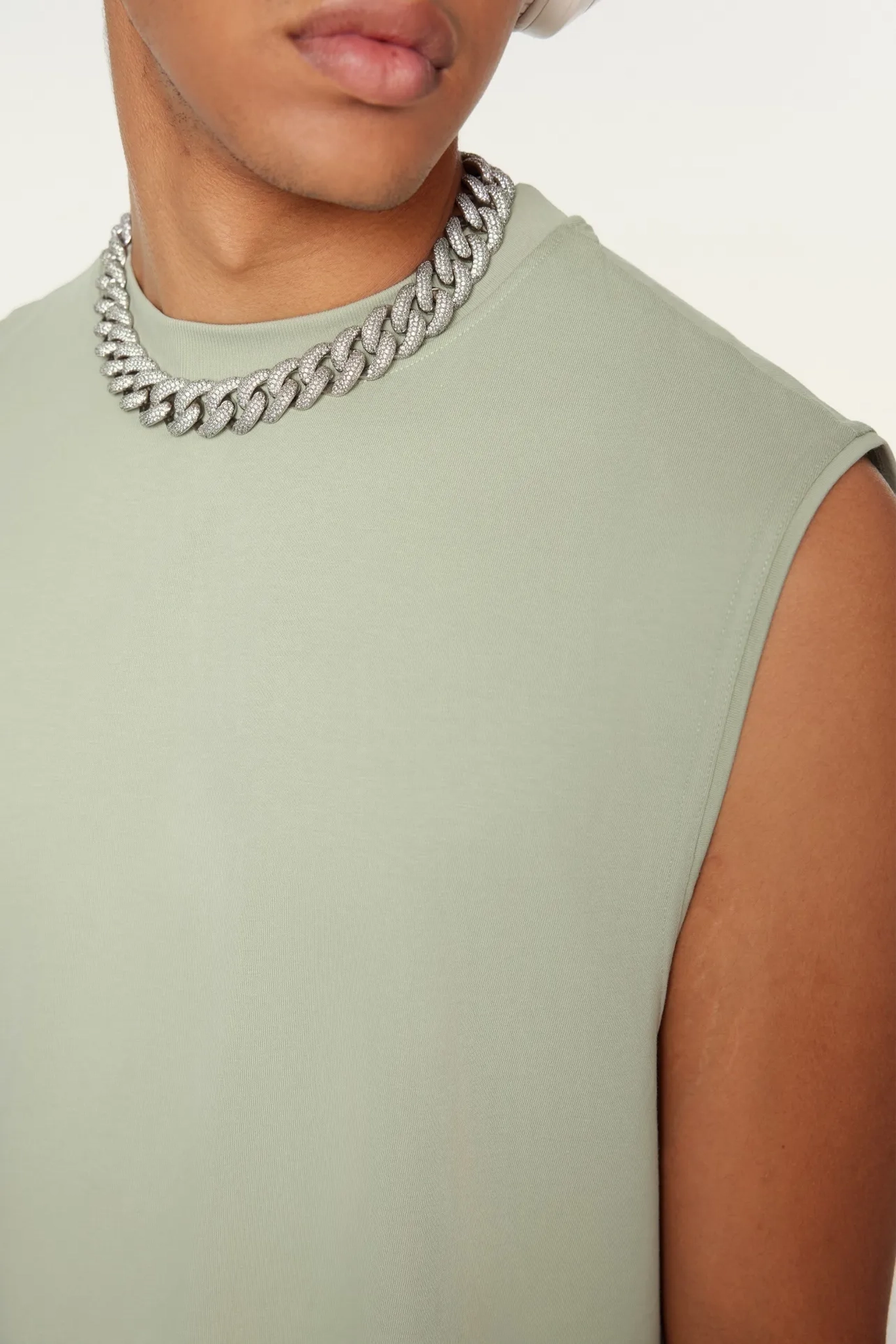 Person wearing a light green sleeveless top and silver chain necklace on a plain background