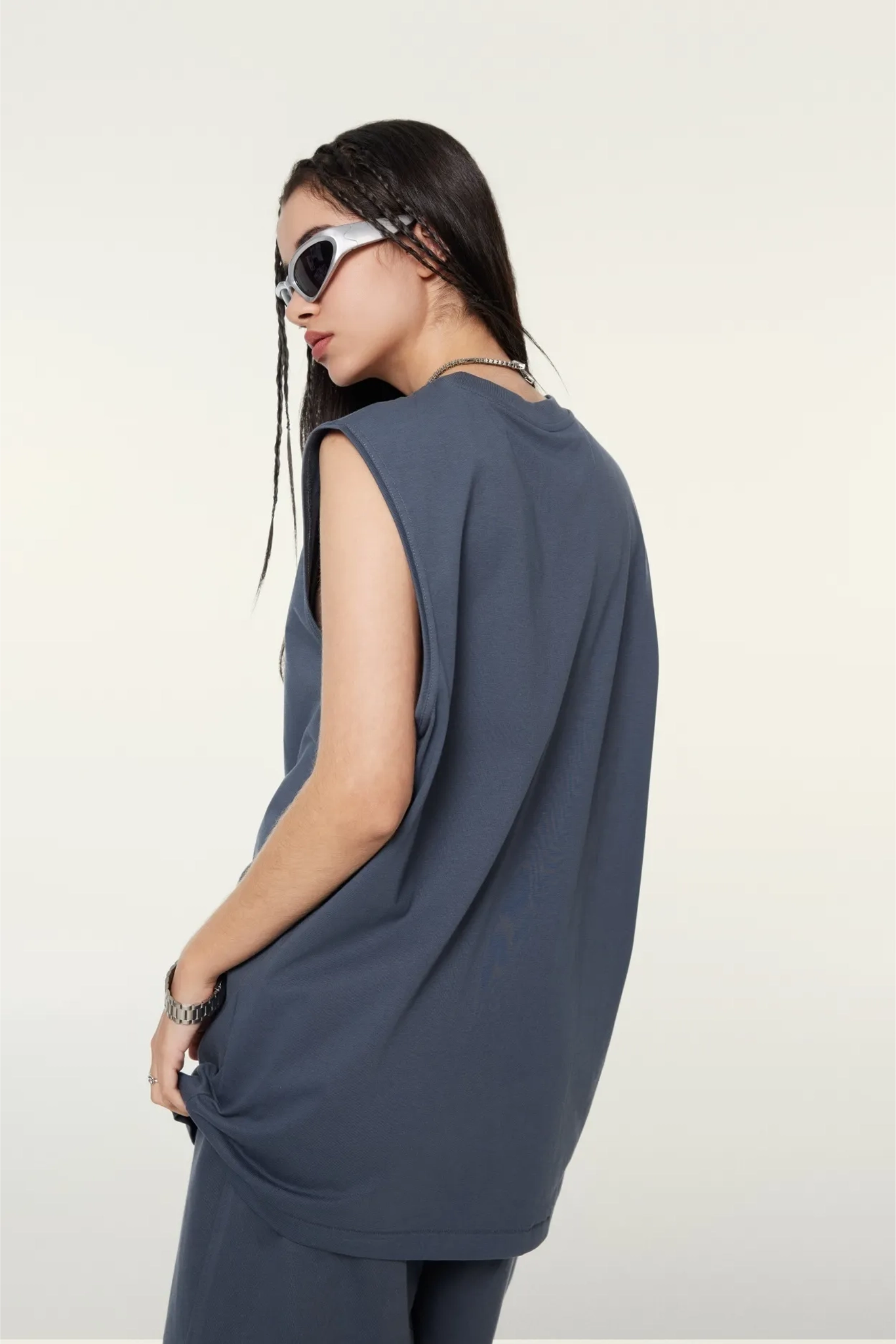 Woman wearing a sleeveless blue top and sunglasses on a white background