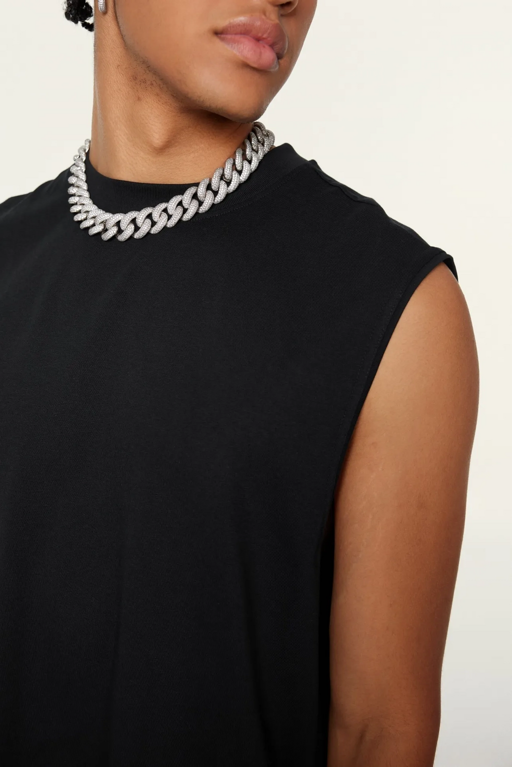 Person wearing a black sleeveless top with a white chain necklace on a neutral background