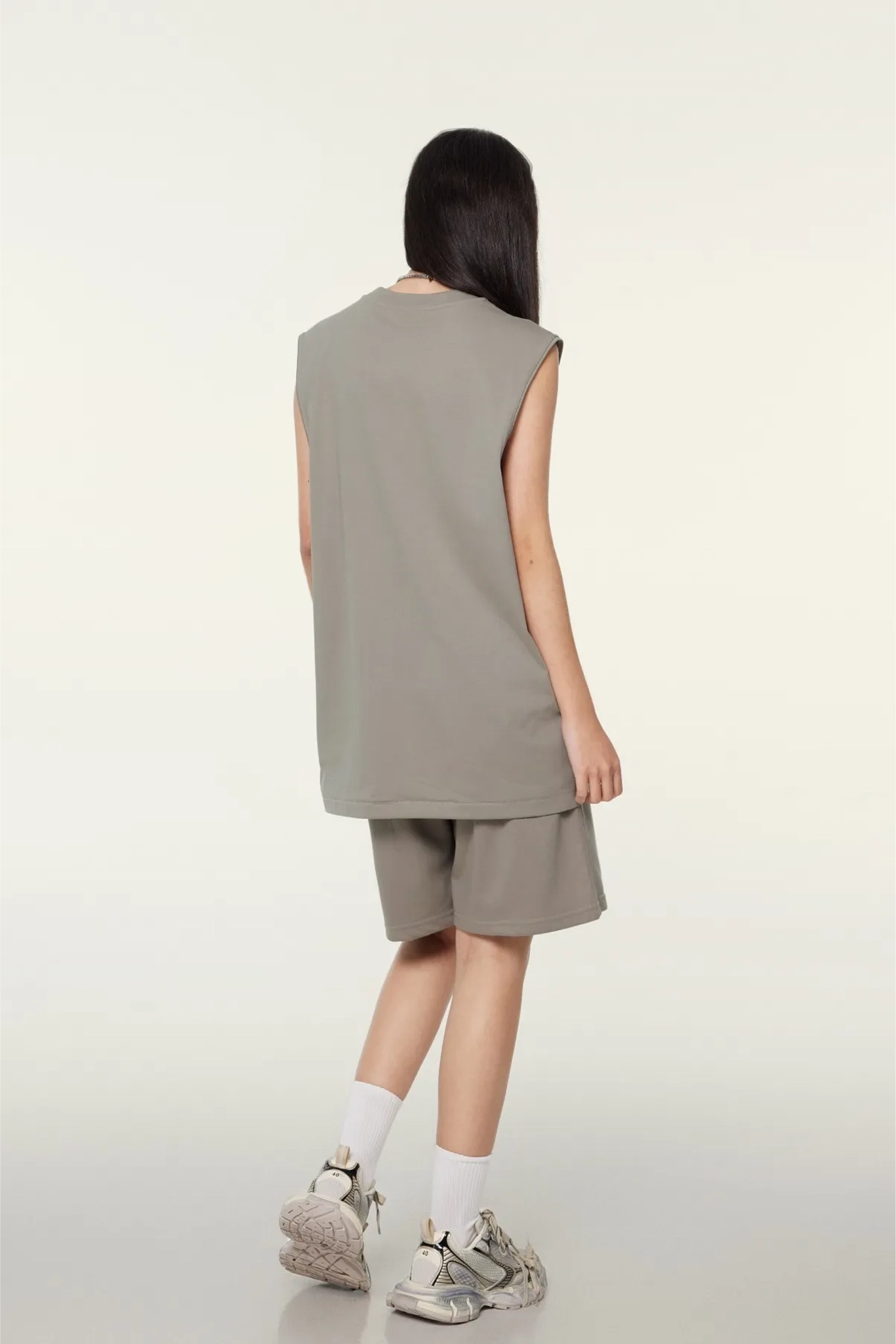 Person wearing a sleeveless beige top and shorts on a white background