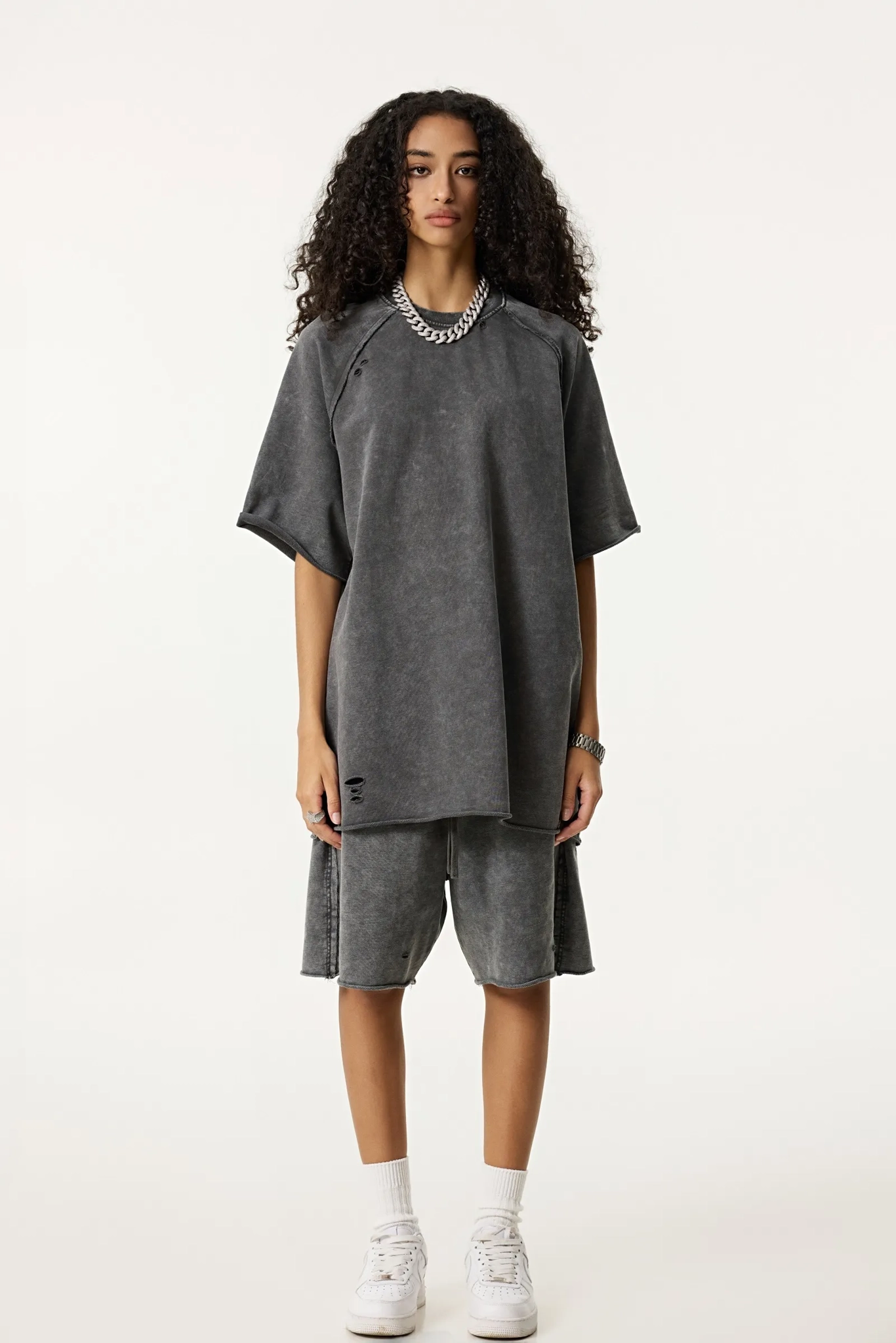 Person wearing a gray oversized top and shorts set on a white background