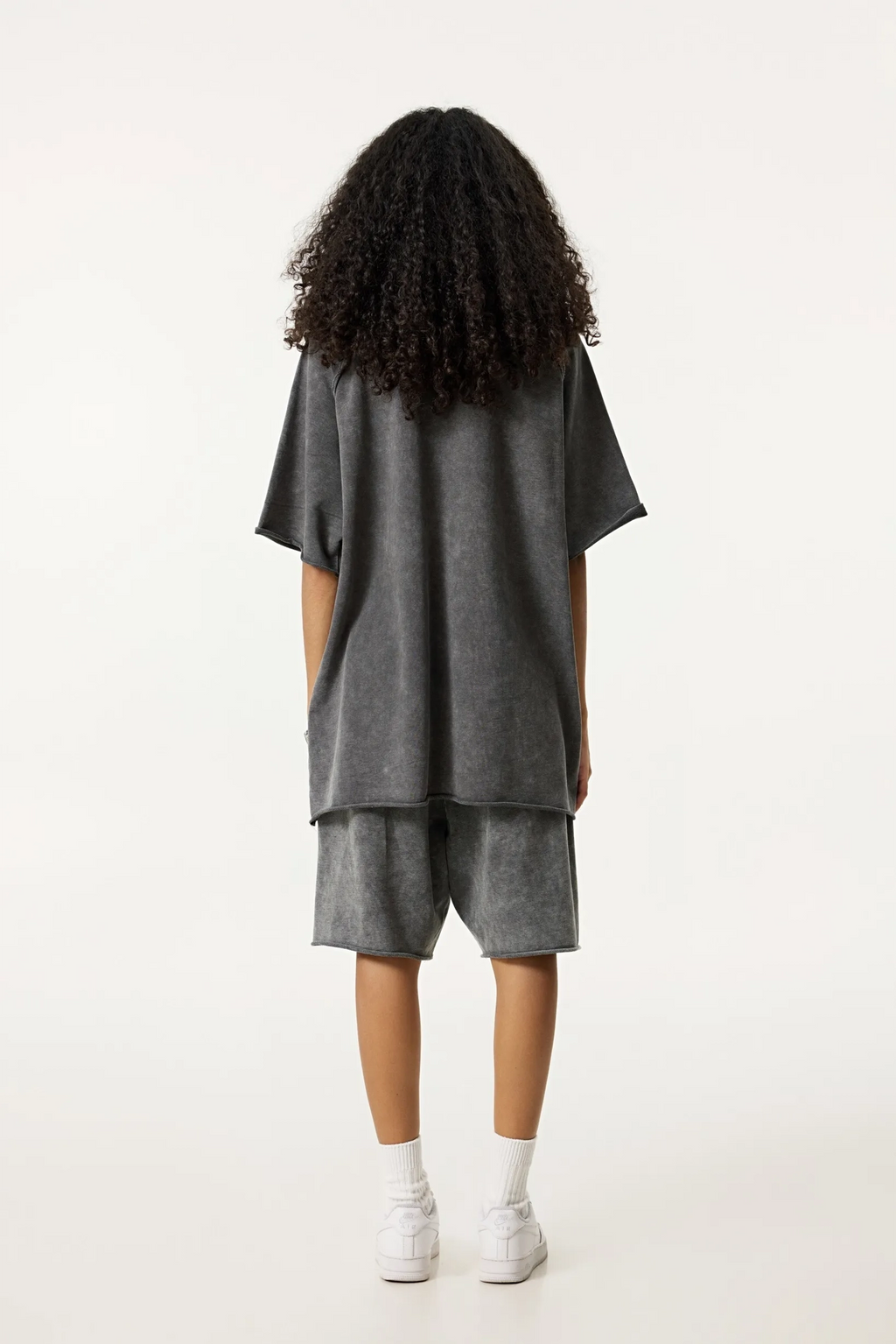 Person wearing a gray oversized t-shirt and shorts set on a white background