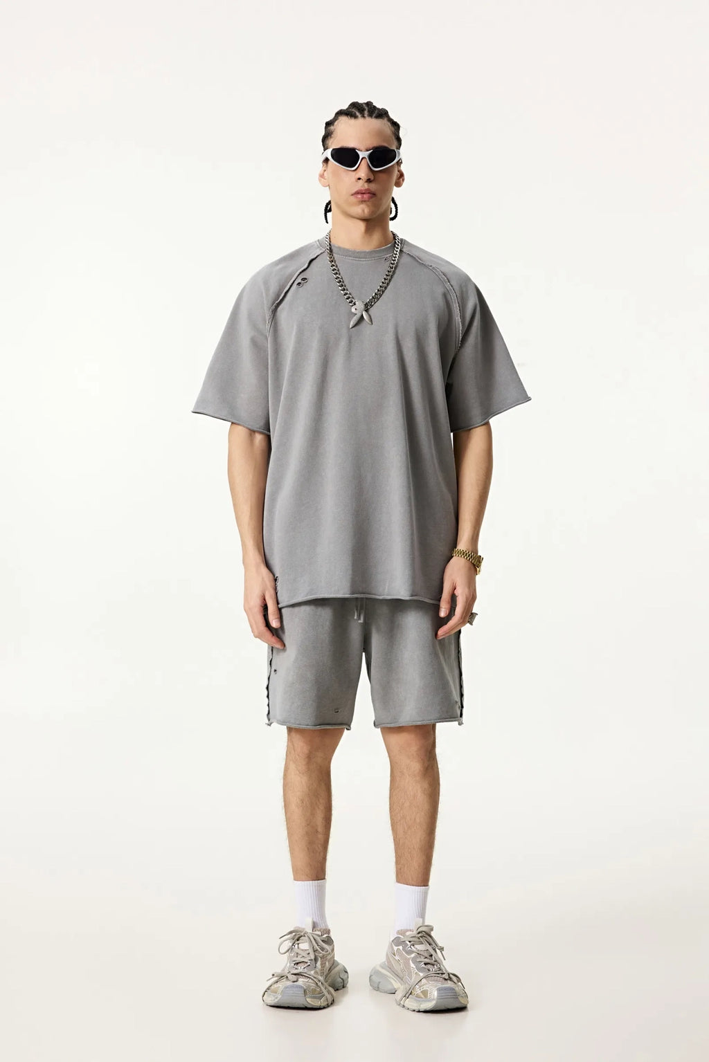 Person wearing a gray oversized t-shirt and shorts with sneakers on a white background