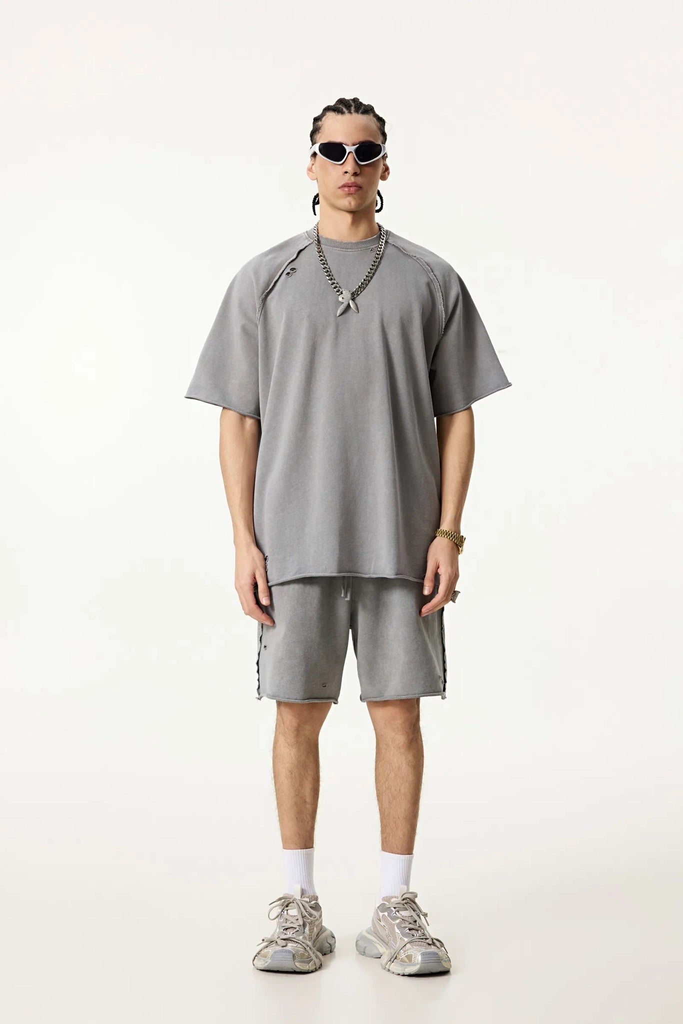 Person wearing a gray oversized t-shirt and shorts with sneakers on a white background