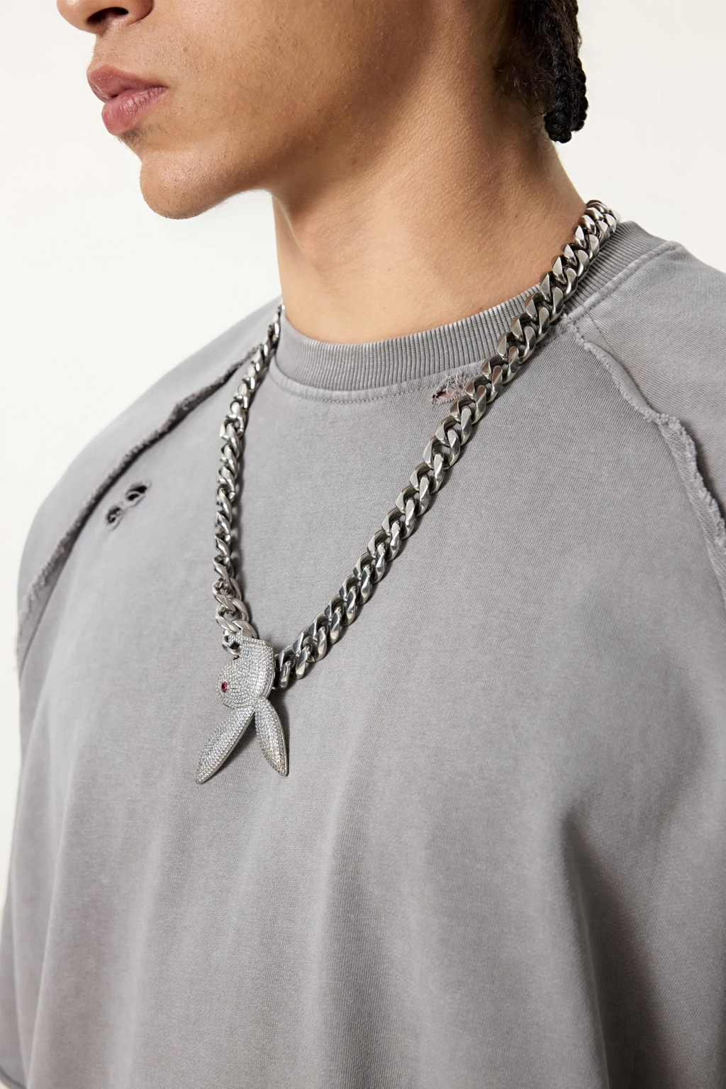 Person wearing a gray sweatshirt with a prominent chain necklace featuring a shark tooth pendant.