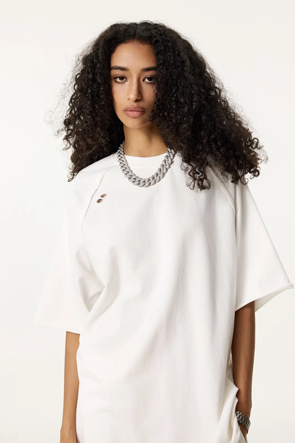 Woman wearing a white oversized shirt with a chain necklace on a plain background