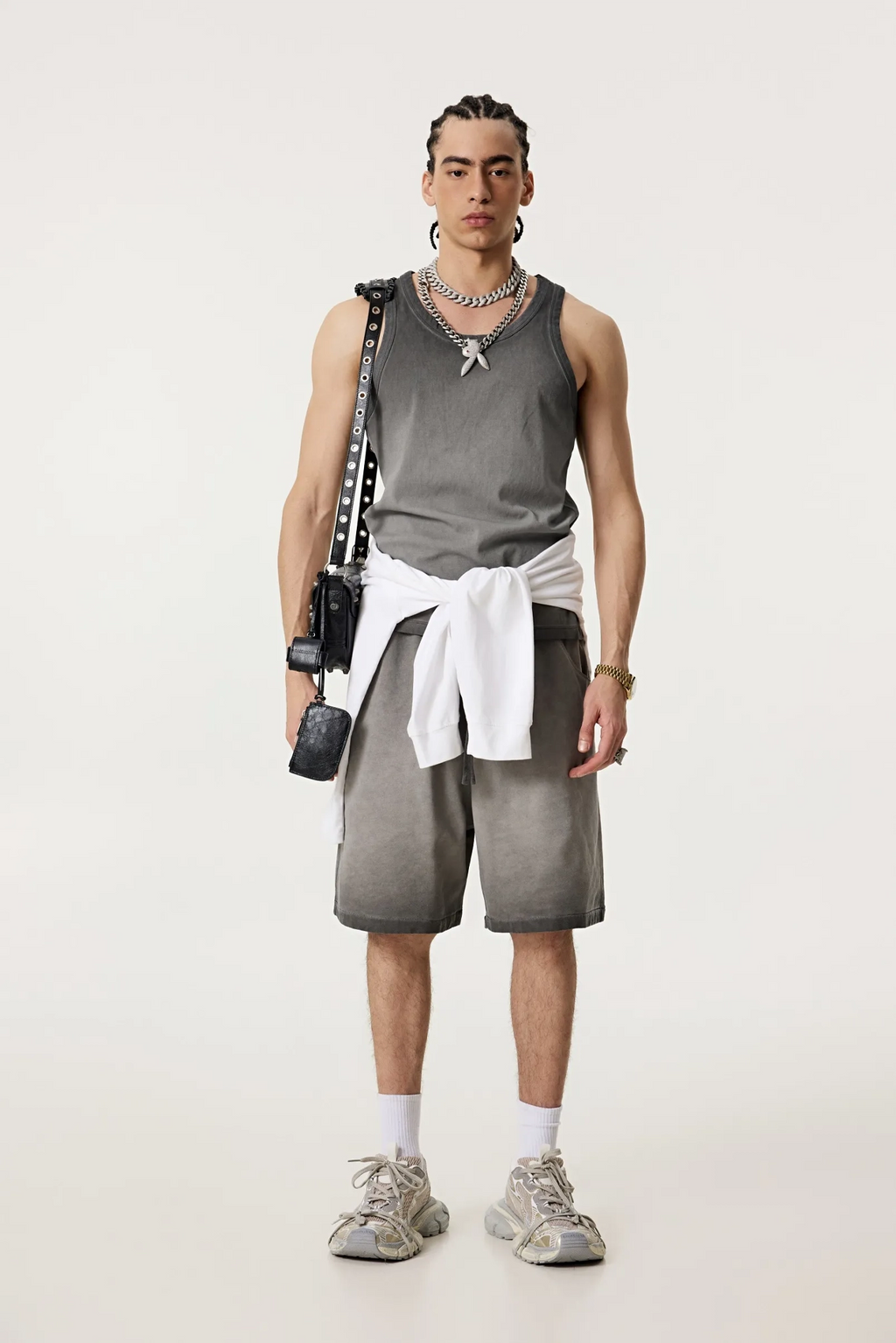 Person wearing a gray tank top and shorts with a white towel, standing against a plain background.